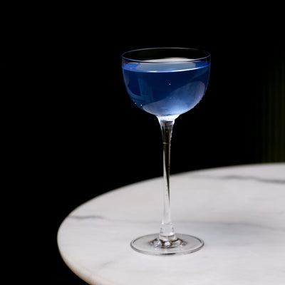 Blue cocktail in a tall glass on a marble surface with a dark background