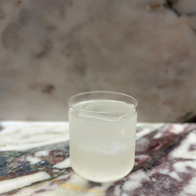 Clear glass of liquid on a marble surface with a marble background ready to drink cocktails